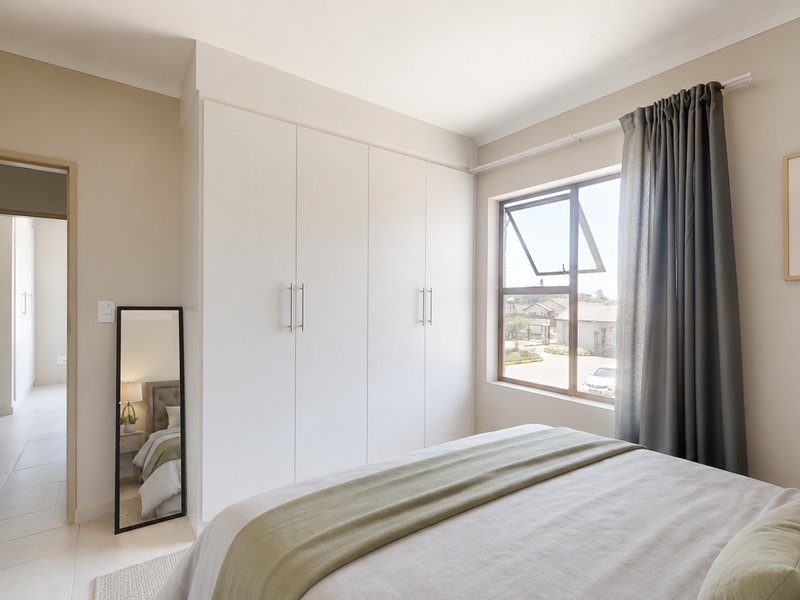 A well-maintained bedroom featuring neutral walls, tiled flooring, and ample built-in cupboard storage with natural light from a casement window.