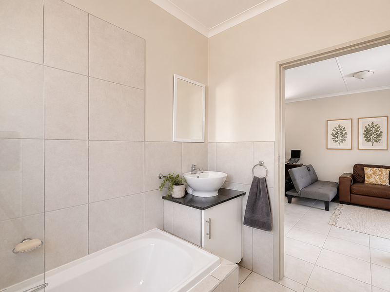 A clean, functional bathroom featuring a bathtub with a glass screen, a modern vessel sink on a vanity cabinet, and neutral wall tiling.