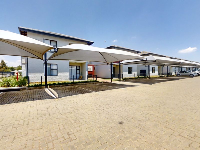 Exterior view of the apartment complex featuring a paved parking area with installed shade sail carports and well-maintained brick building facades.