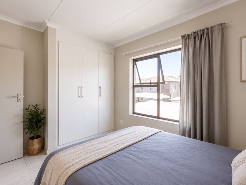 A well-maintained bedroom featuring neutral walls, built-in cupboards, and a large window providing natural light.