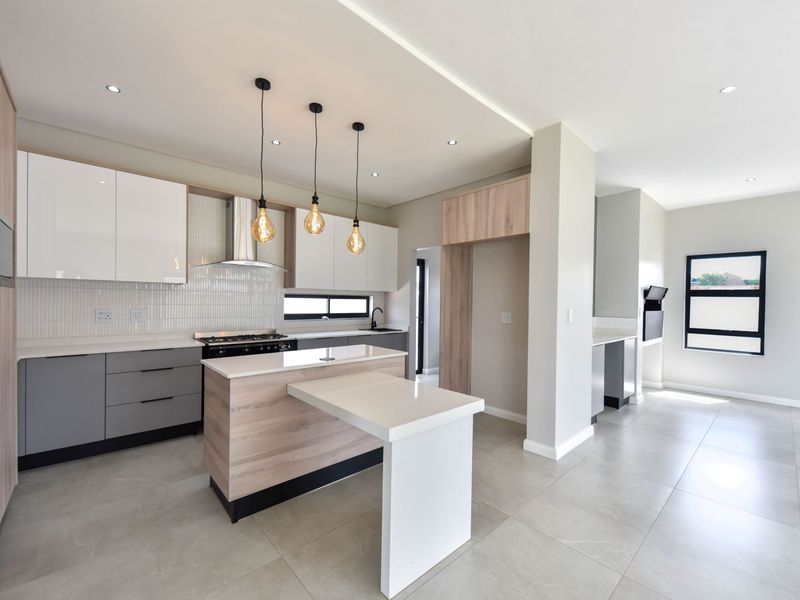 Modern kitchen featuring sleek two-tone cabinetry, stone countertops, a central island, and high-quality built-in appliances with neutral tiled flooring throughout.