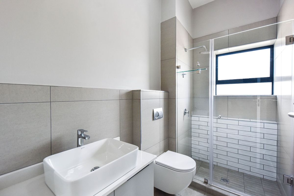 Modern bathroom featuring a wall-mounted toilet, glass-enclosed shower with subway tile accents, and a contemporary vessel sink vanity.