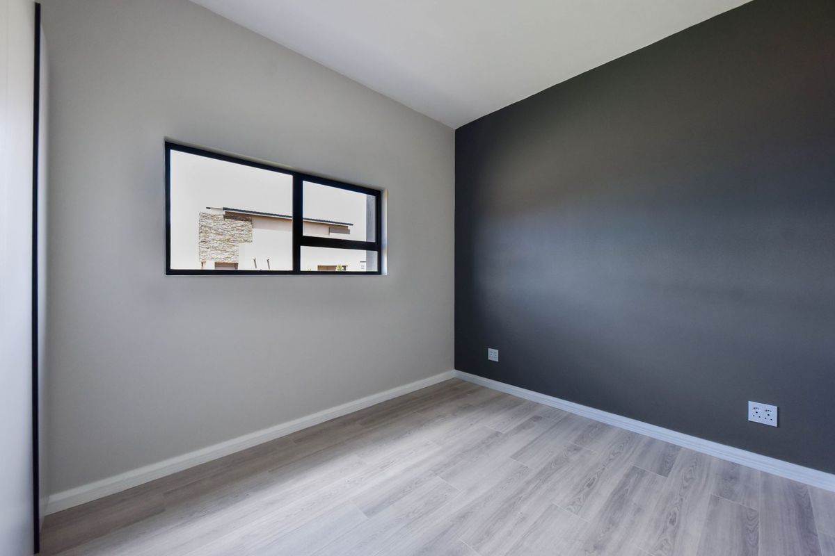 A clean, modern, and empty bedroom featuring light wood-look laminate flooring, a contrasting dark accent wall, and a contemporary aluminium-framed window.