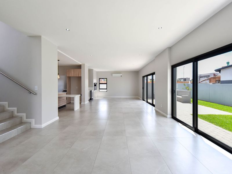 Spacious open-plan living area featuring large format floor tiles, modern staircase, and expansive sliding glass doors leading to the outdoor patio.