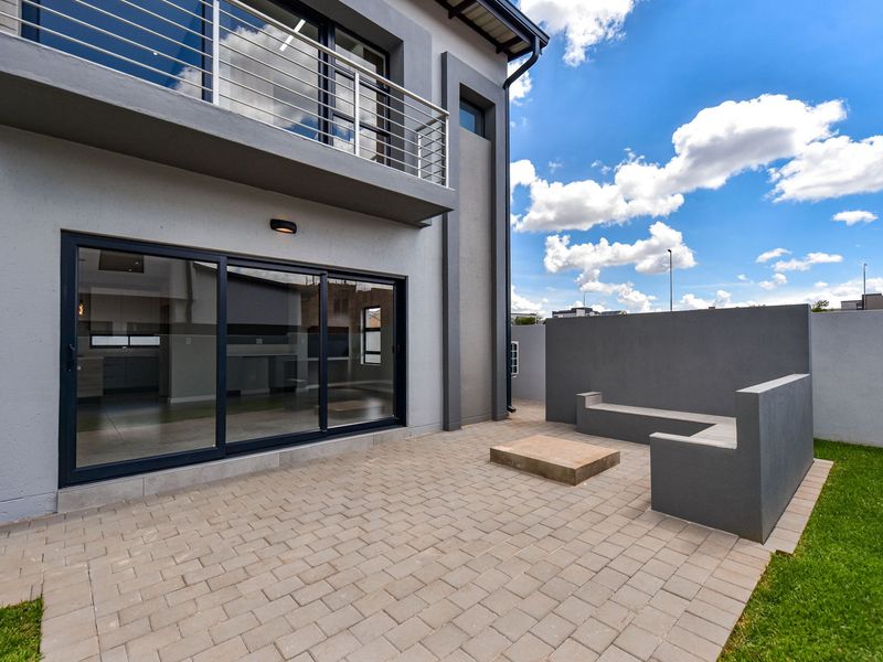 Modern rear exterior featuring a paved patio, built-in concrete seating, and a balcony with stainless steel railings overlooking the garden area.