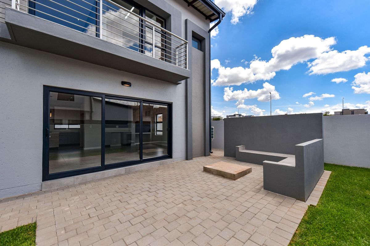 Modern rear exterior featuring a paved patio, built-in concrete seating, and a balcony with stainless steel railings overlooking the garden area.