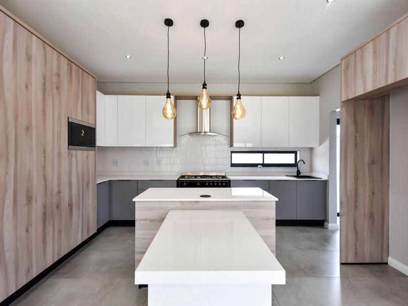 Modern kitchen featuring sleek two-tone cabinetry, a central island with integrated breakfast bar, quartz countertops, and high-end built-in appliances.