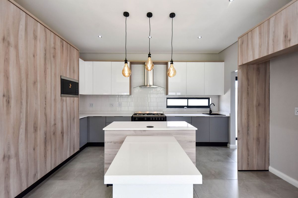 Modern kitchen featuring sleek two-tone cabinetry, a central island with integrated breakfast bar, quartz countertops, and high-end built-in appliances.