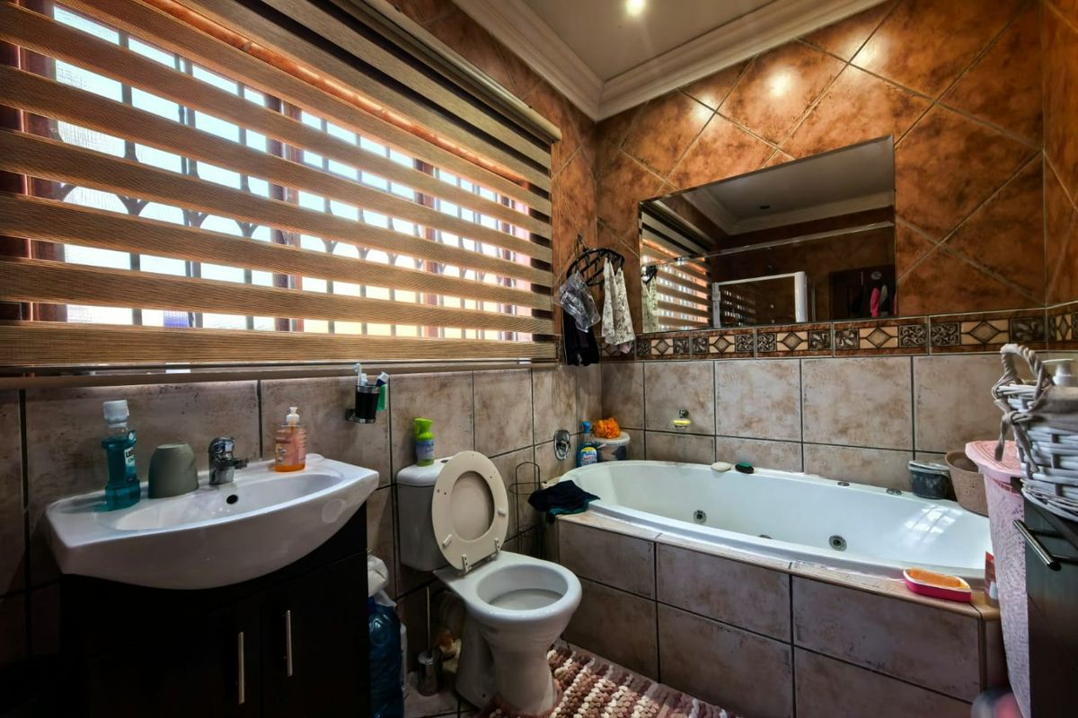 A functional bathroom featuring a built-in bathtub, vanity basin, toilet, and tiled wall finishes with integrated lighting.