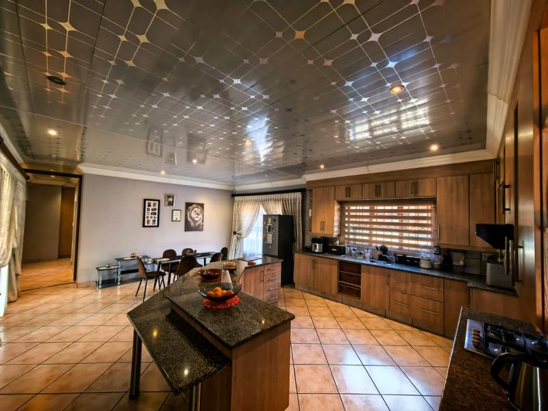 Spacious open-plan kitchen and dining area featuring granite countertops, extensive wooden cabinetry, and unique decorative ceiling panels with integrated lighting.