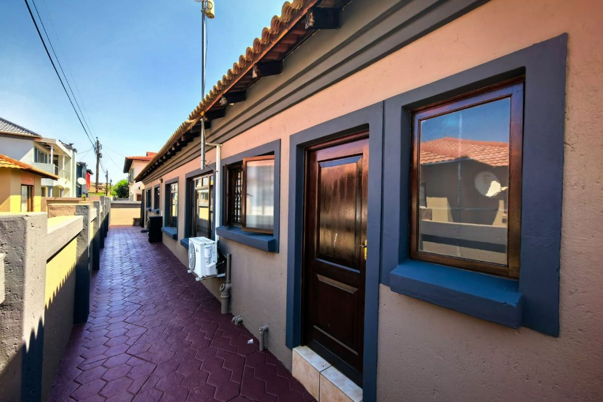 A side exterior view of the property featuring a paved walkway, timber door and window frames, and a terracotta tiled roof.