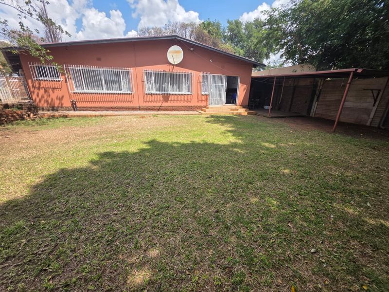 Rear view of the house featuring a spacious lawn, covered patio area, and exterior brick facade with security bars on windows.