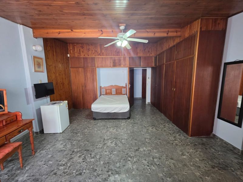 Spacious bedroom featuring extensive built-in wooden cabinetry, a classic wooden ceiling with a ceiling fan, and durable tiled flooring.