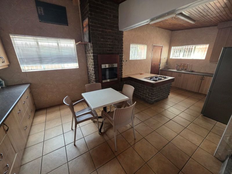 Spacious kitchen featuring a central island with hob, built-in oven, brick fireplace, and ample cabinetry, finished with tiled flooring and a wooden ceiling.