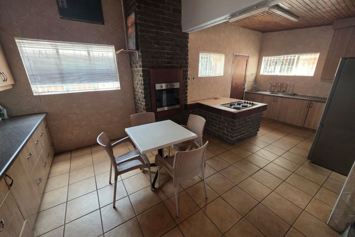 Spacious kitchen featuring a central island with hob, built-in oven, brick fireplace, and ample cabinetry, finished with tiled flooring and a wooden ceiling.