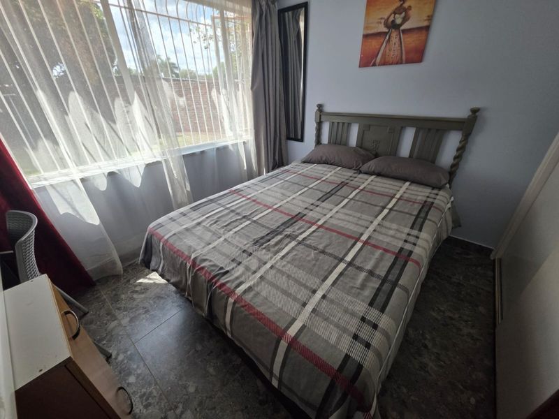 A functional bedroom featuring tiled flooring and a window fitted with security bars, providing natural light and basic security.