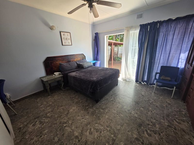Spacious bedroom featuring tiled flooring, a ceiling fan, and direct access to the outdoor area through a sliding glass door.