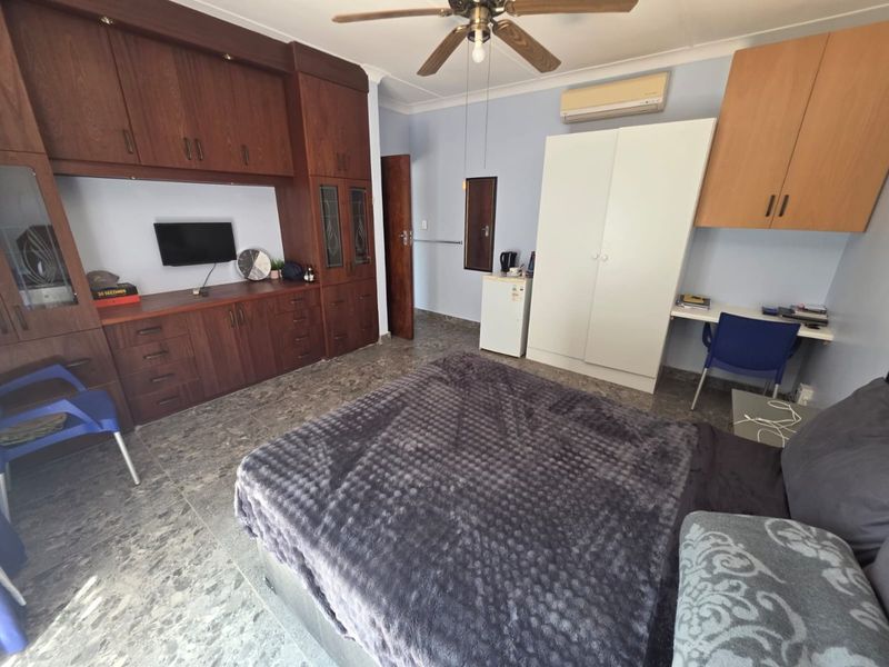 A bedroom featuring extensive built-in wooden cabinetry, tiled flooring, a ceiling fan, and a wall-mounted air conditioning unit.