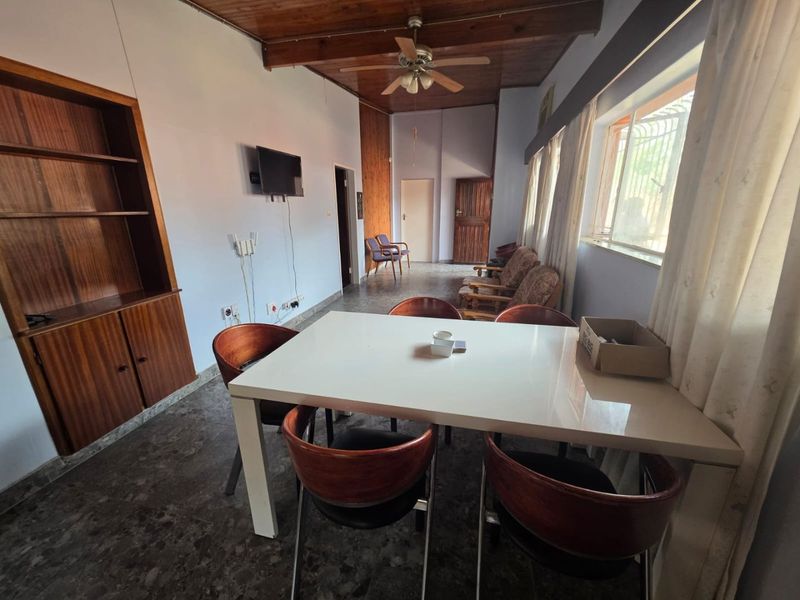 A living area featuring a wooden ceiling with a fan, built-in shelving, and tiled flooring, offering a dated but functional space.