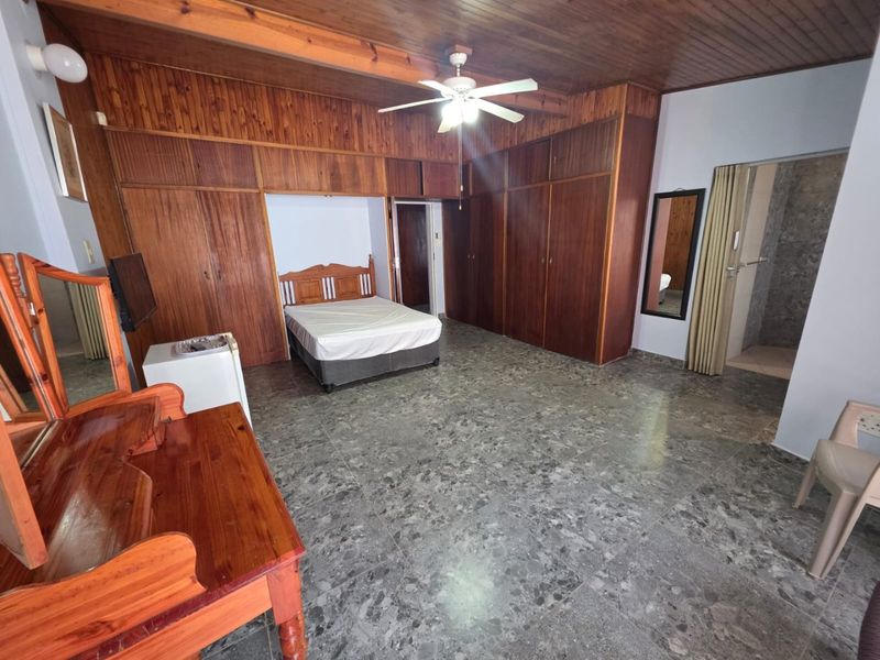 Spacious bedroom featuring extensive built-in wooden cabinetry, a timber-clad ceiling with a central fan, and durable tiled flooring throughout.