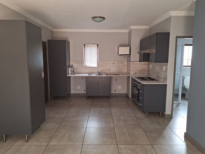Modern kitchen featuring grey built-in cabinetry, tiled flooring, a stainless steel sink, and integrated electric cooking appliances with a tiled backsplash.