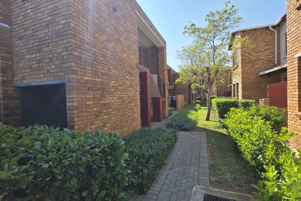 Exterior view of a face brick apartment complex featuring a paved walkway and well-maintained garden hedges.