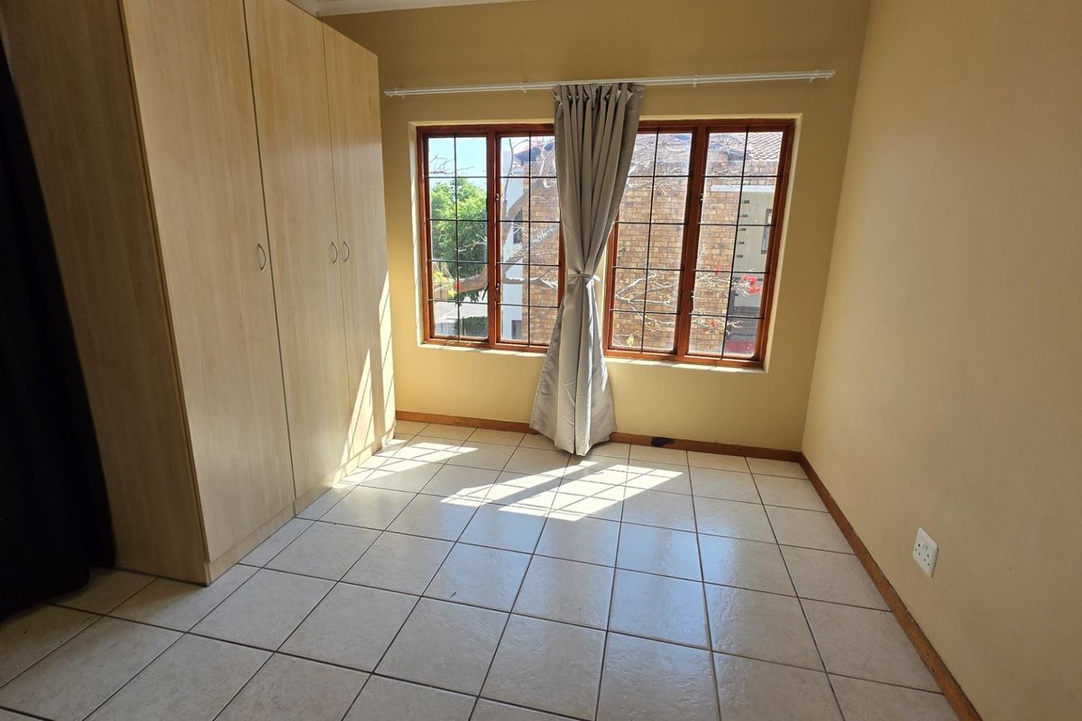 A bright, empty bedroom featuring tiled flooring, built-in wooden cupboards, and large windows with natural light.