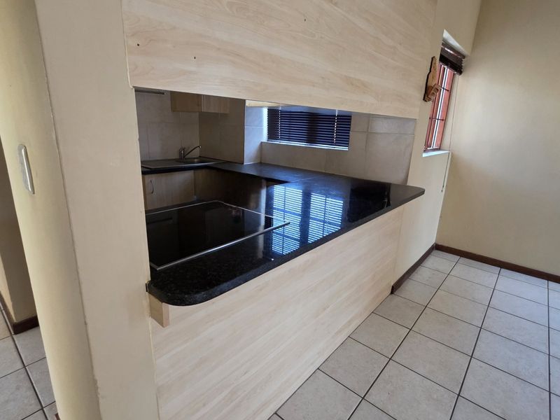 A clean, functional kitchen featuring light wood-finish cabinetry, dark granite countertops, an integrated electric hob, and neutral tiled flooring.