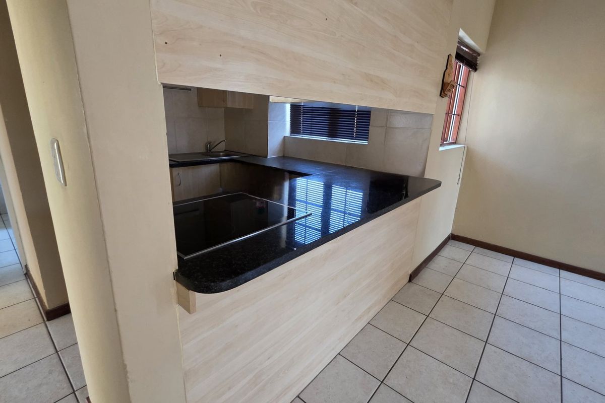 A clean, functional kitchen featuring light wood-finish cabinetry, dark granite countertops, an integrated electric hob, and neutral tiled flooring.