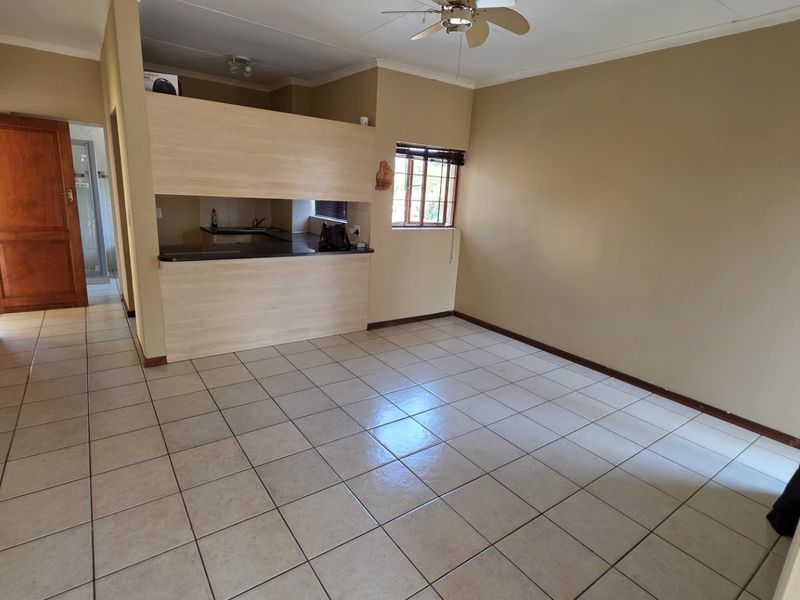 An open-plan living area featuring tiled flooring, a ceiling fan, and a breakfast bar connecting to the kitchen space.