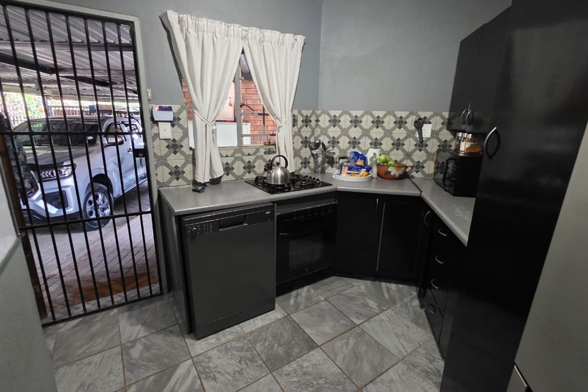 Compact kitchen featuring dark cabinetry, tiled backsplash, gas hob, built-in oven, and direct access to the exterior via a security gate.