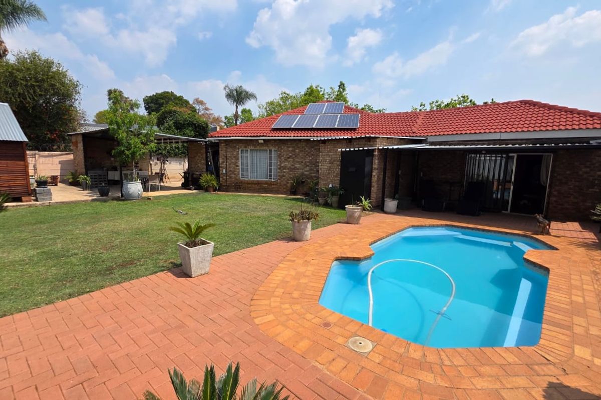 Rear view of the property featuring a swimming pool, brick paved patio area, well-maintained lawn, and solar panels installed on the tiled roof.