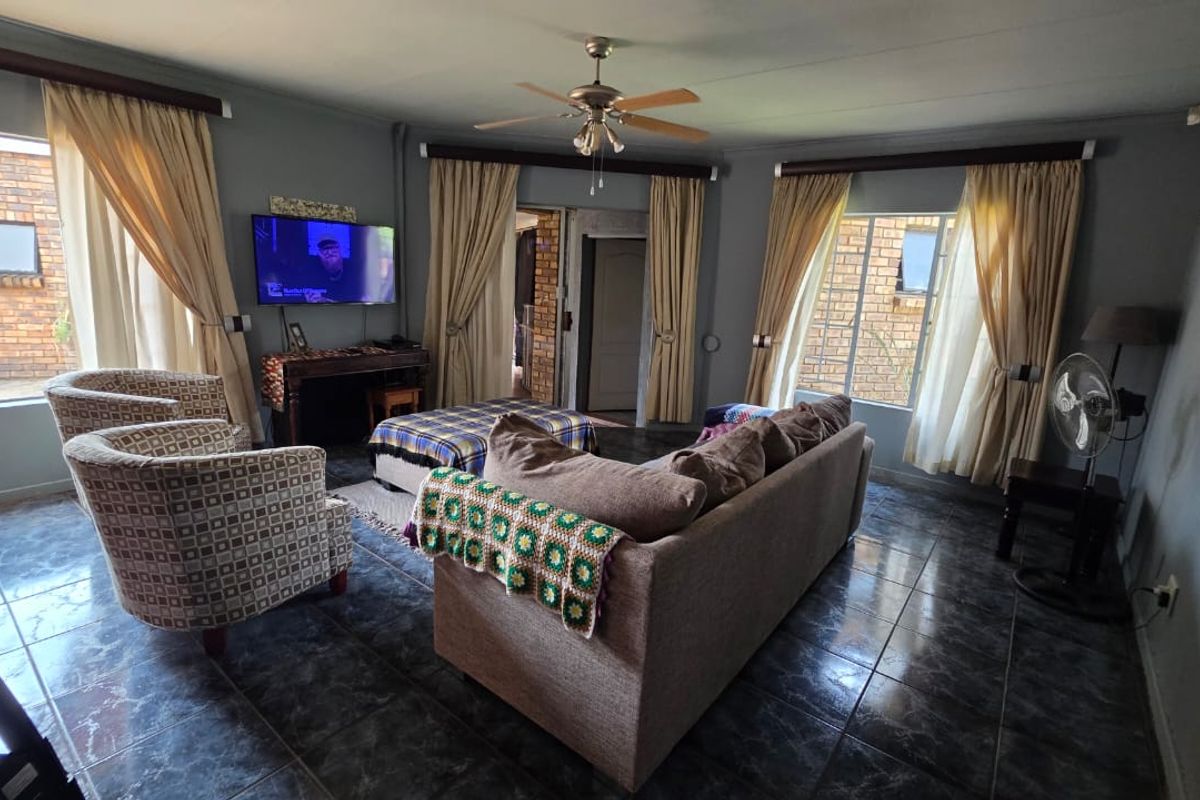 A spacious living room featuring dark tiled flooring, a ceiling fan, and large windows that provide natural light and views of the exterior brickwork.