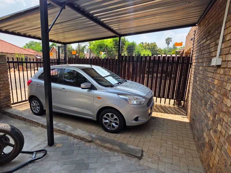 A covered carport area featuring paved flooring, brick walling, and secure perimeter fencing.