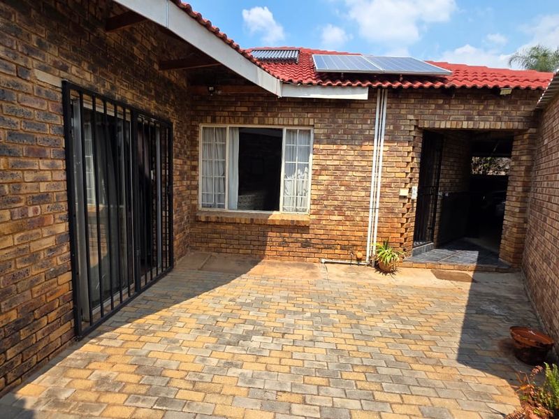 A private rear courtyard featuring face brick walls, a paved patio area, and roof-mounted solar panels.