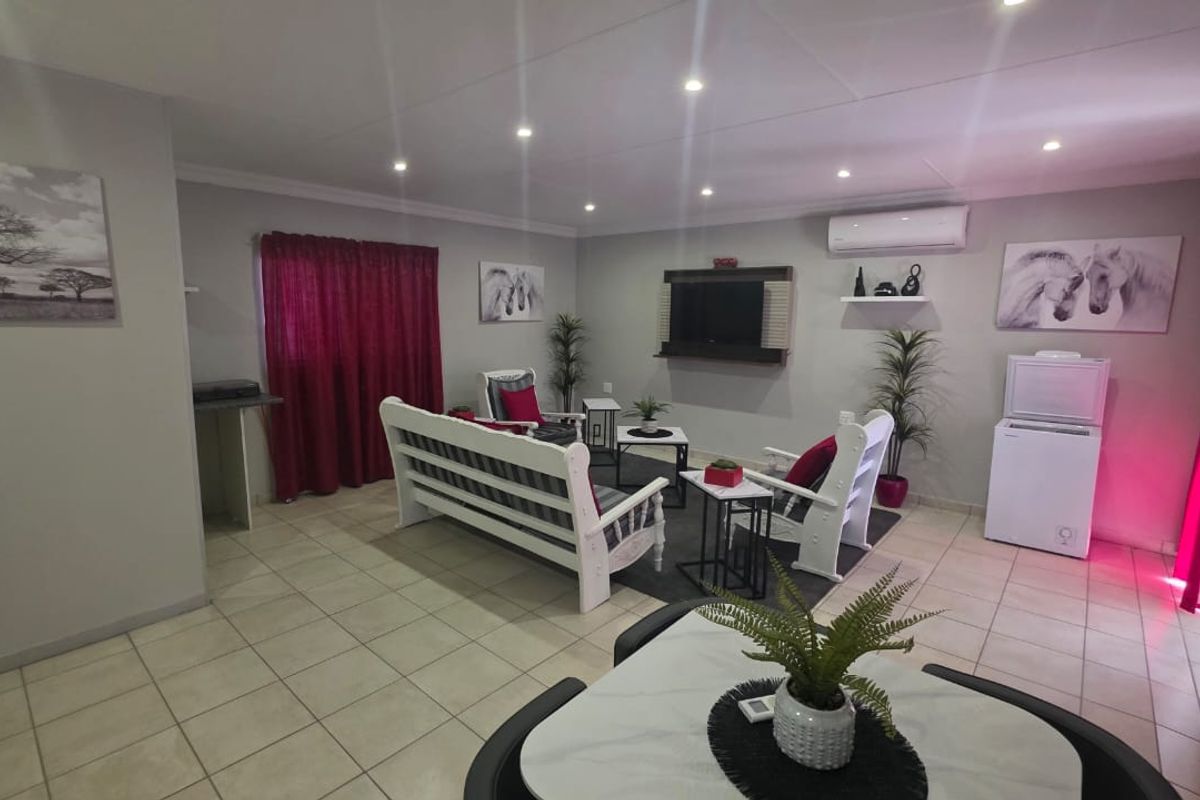 A spacious living room featuring tiled flooring, recessed downlighting, and a wall-mounted air conditioning unit, offering a comfortable and functional living space.