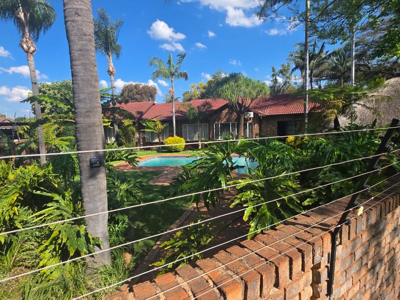 Rear view of the property featuring a swimming pool, landscaped garden, and brick boundary wall with electric fencing.