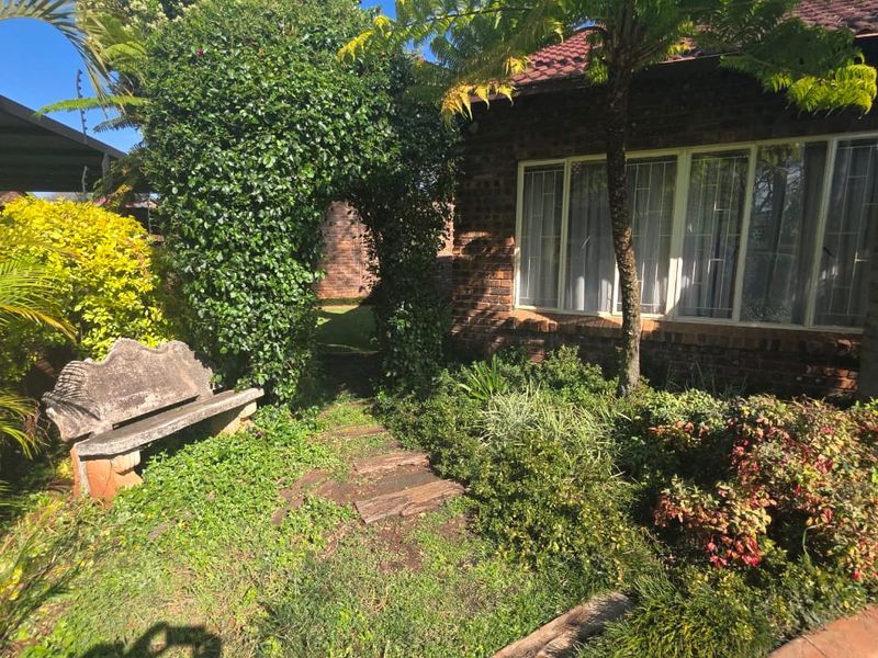 A lush, established garden area featuring a brick exterior facade, mature greenery, and a stone bench set against the side of the house.