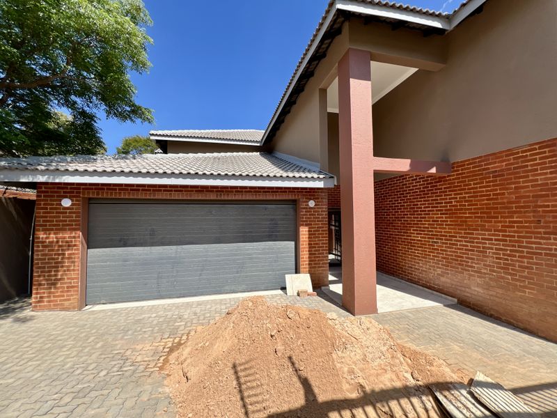 Front exterior view of the property featuring a brick facade, tiled roof, and an automated garage door with a paved driveway.