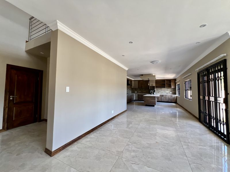 Spacious open-plan living area featuring a modern kitchen with island, tiled flooring, and neutral finishes, offering a bright and versatile layout.