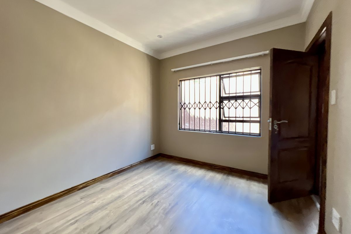 A clean, empty bedroom featuring light-toned laminate flooring, neutral wall paint, and a window fitted with security bars.