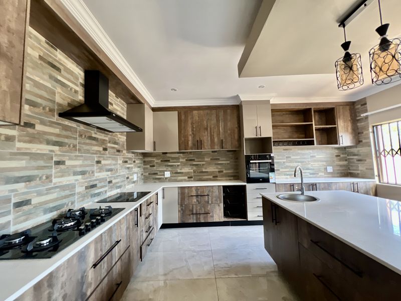 Modern kitchen featuring wood-grain cabinetry, stone countertops, a central island, integrated appliances, and a stylish tiled backsplash.