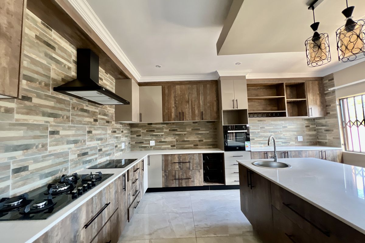 Modern kitchen featuring wood-grain cabinetry, stone countertops, a central island, integrated appliances, and a stylish tiled backsplash.
