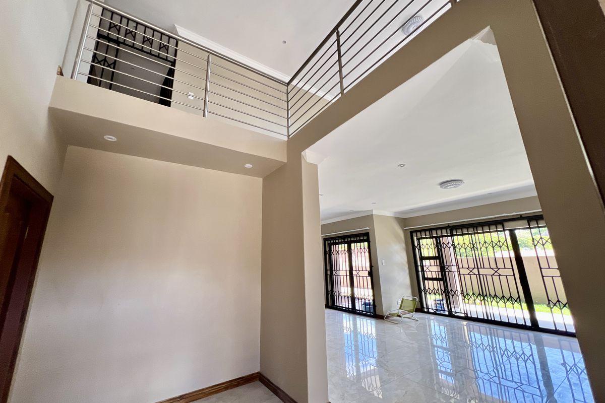 Spacious double-volume living area featuring tiled floors, recessed lighting, and a mezzanine level with a modern stainless steel balustrade, leading to outdoor access.