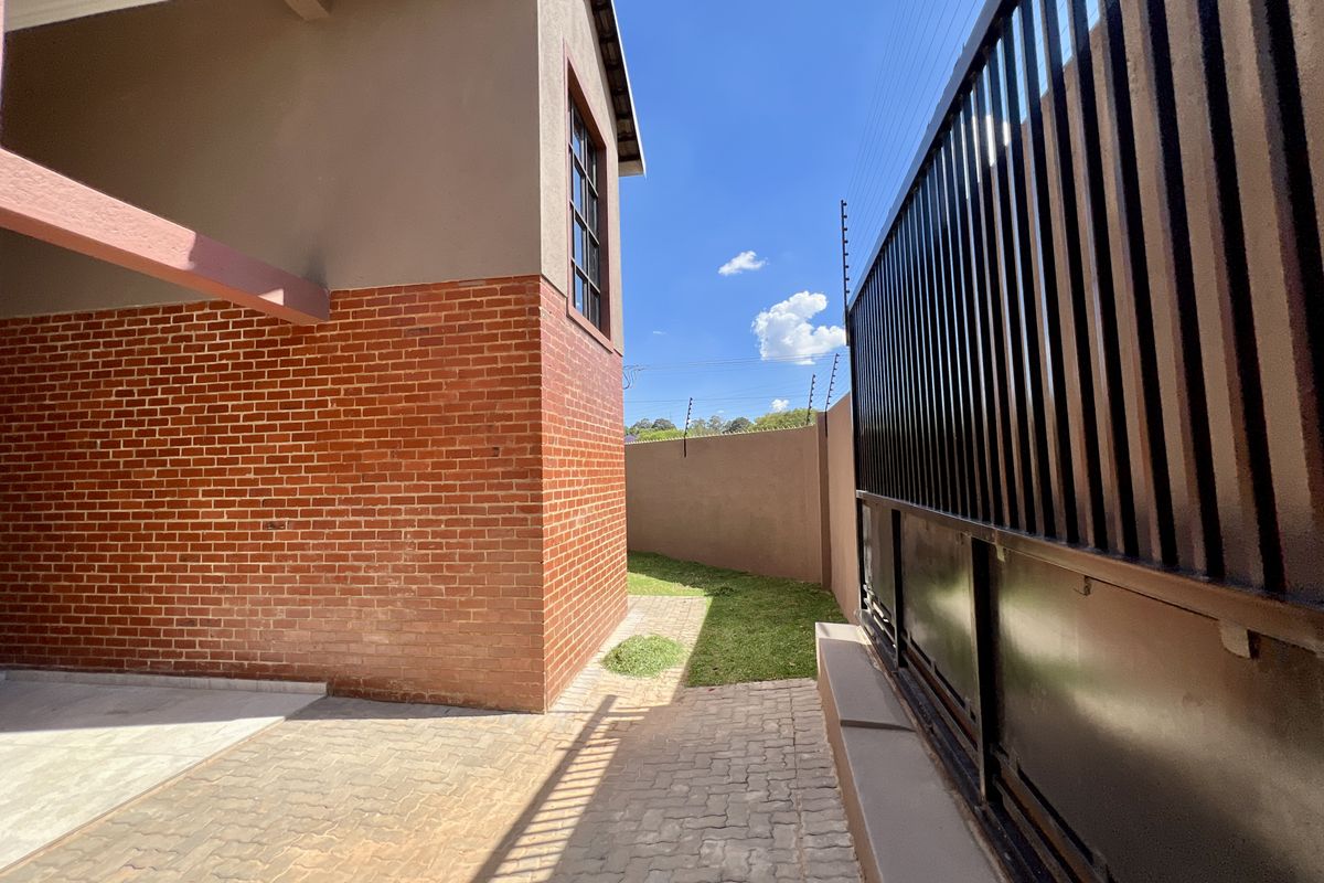 A side view of the property featuring a brick facade, paved driveway, and secure boundary wall with an electric fence.