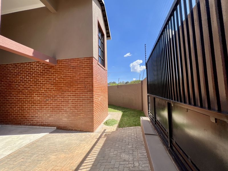 A side view of the property featuring a brick facade, paved driveway, and secure boundary wall with an electric fence.