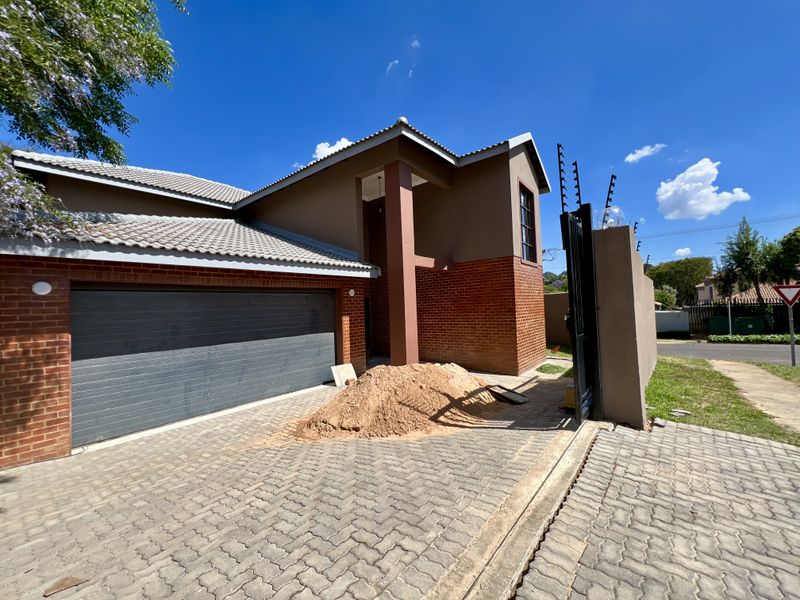 Front exterior view of a modern house featuring a brick facade, tiled roof, double garage, and paved driveway with perimeter security fencing.