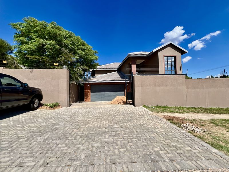 Front view of a modern house featuring a paved driveway, perimeter wall with electric fencing, and a double garage.