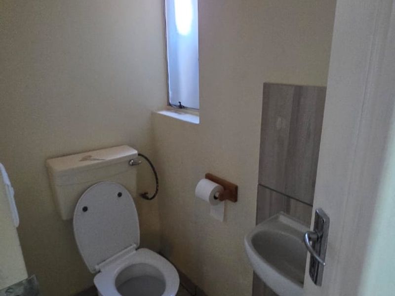 A compact guest bathroom featuring a toilet, wall-mounted basin, and tiled flooring with neutral wall finishes.