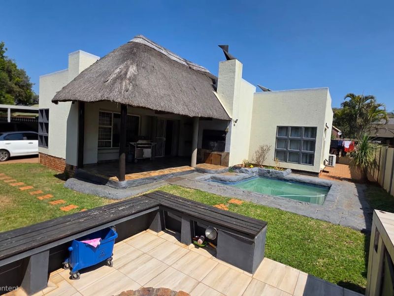 Rear exterior view of a duet property featuring a thatched roof patio, built-in braai area, and a small swimming pool set in a private garden.
